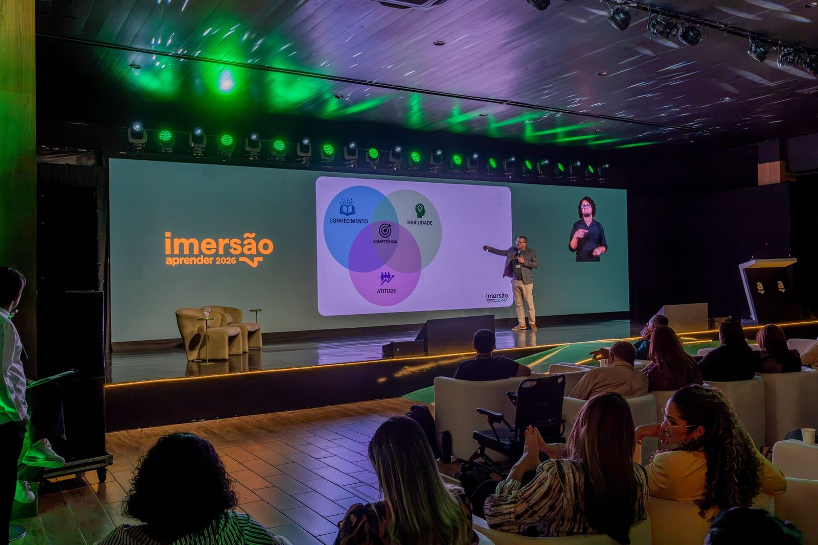 Palestrante no palco com telão e intérprete de libras