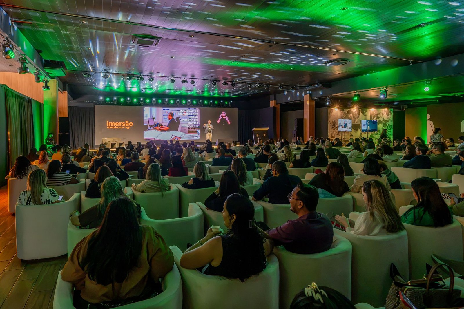 Plateia cheia no auditório iluminado em verde durante a palestra