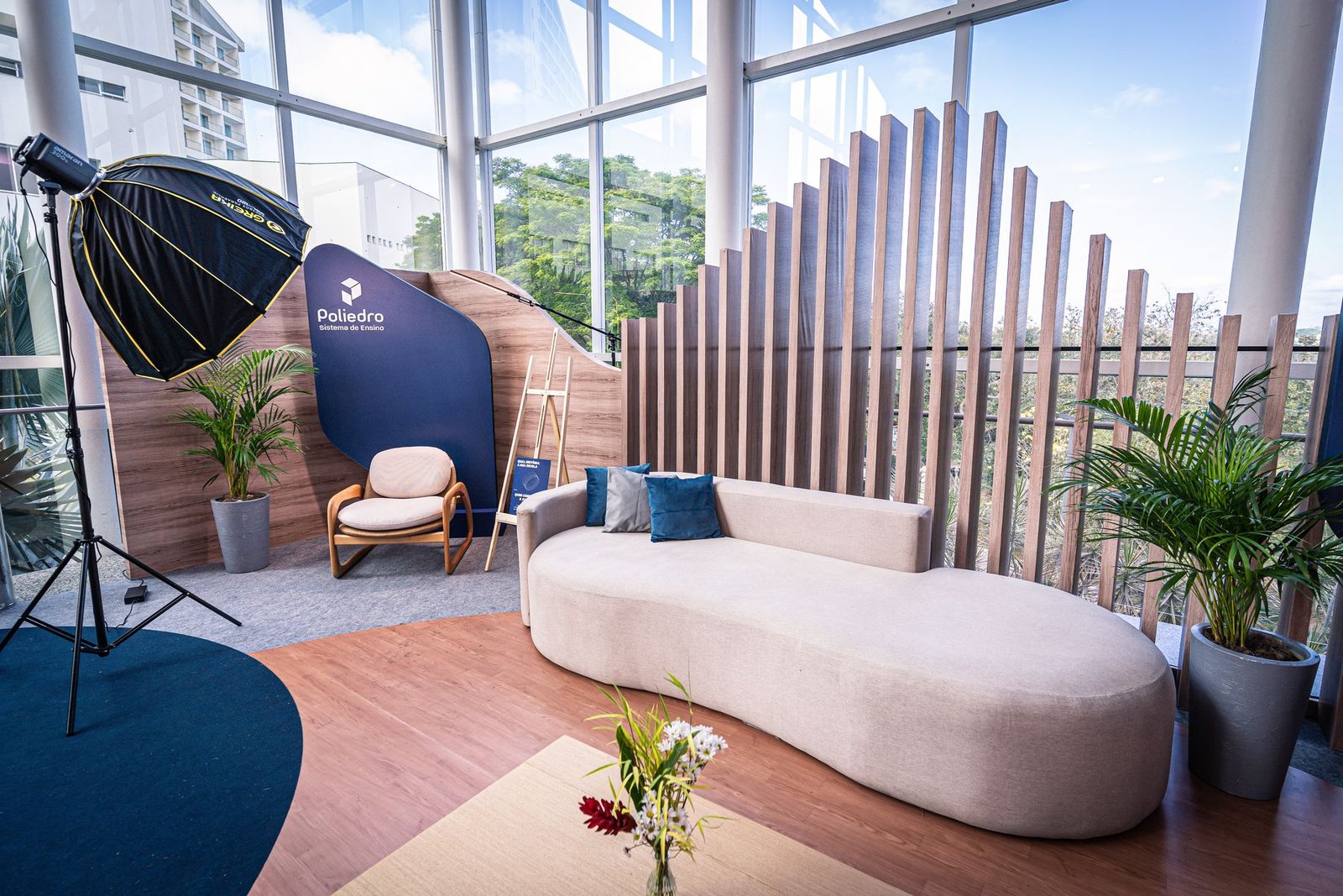 Lounge com sofá curvo claro, ripado de madeira e plantas diante de janela ampla
