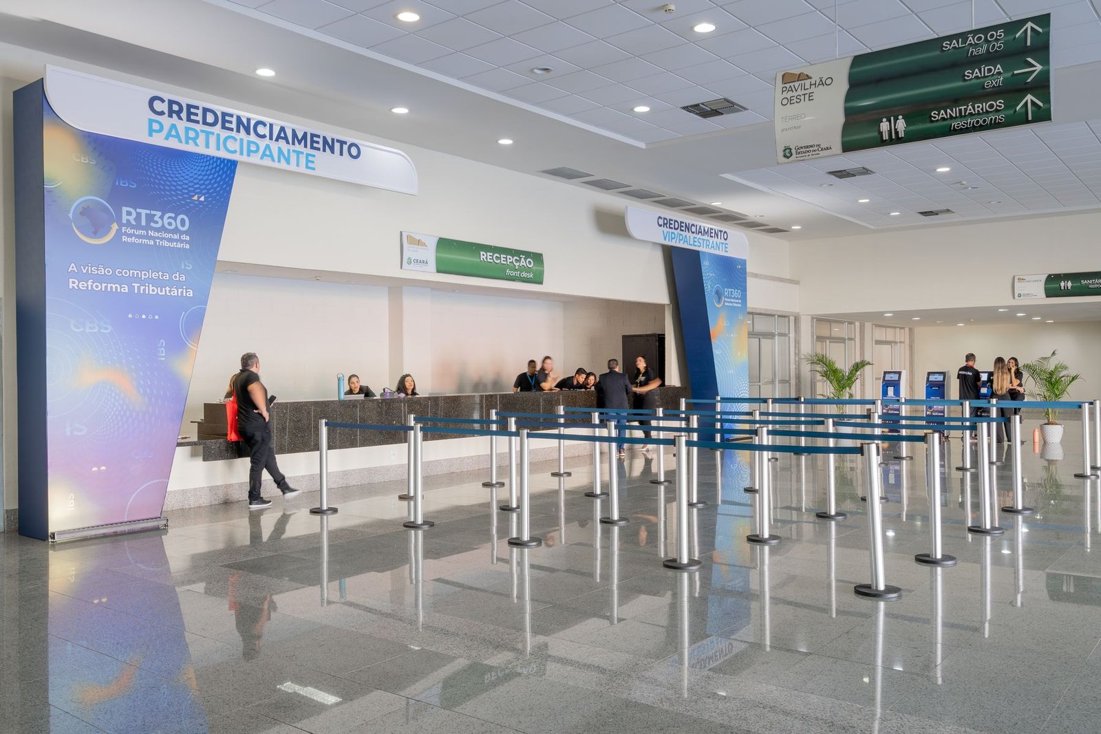 Área de credenciamento de participantes com painéis azuis e organizadores de fila