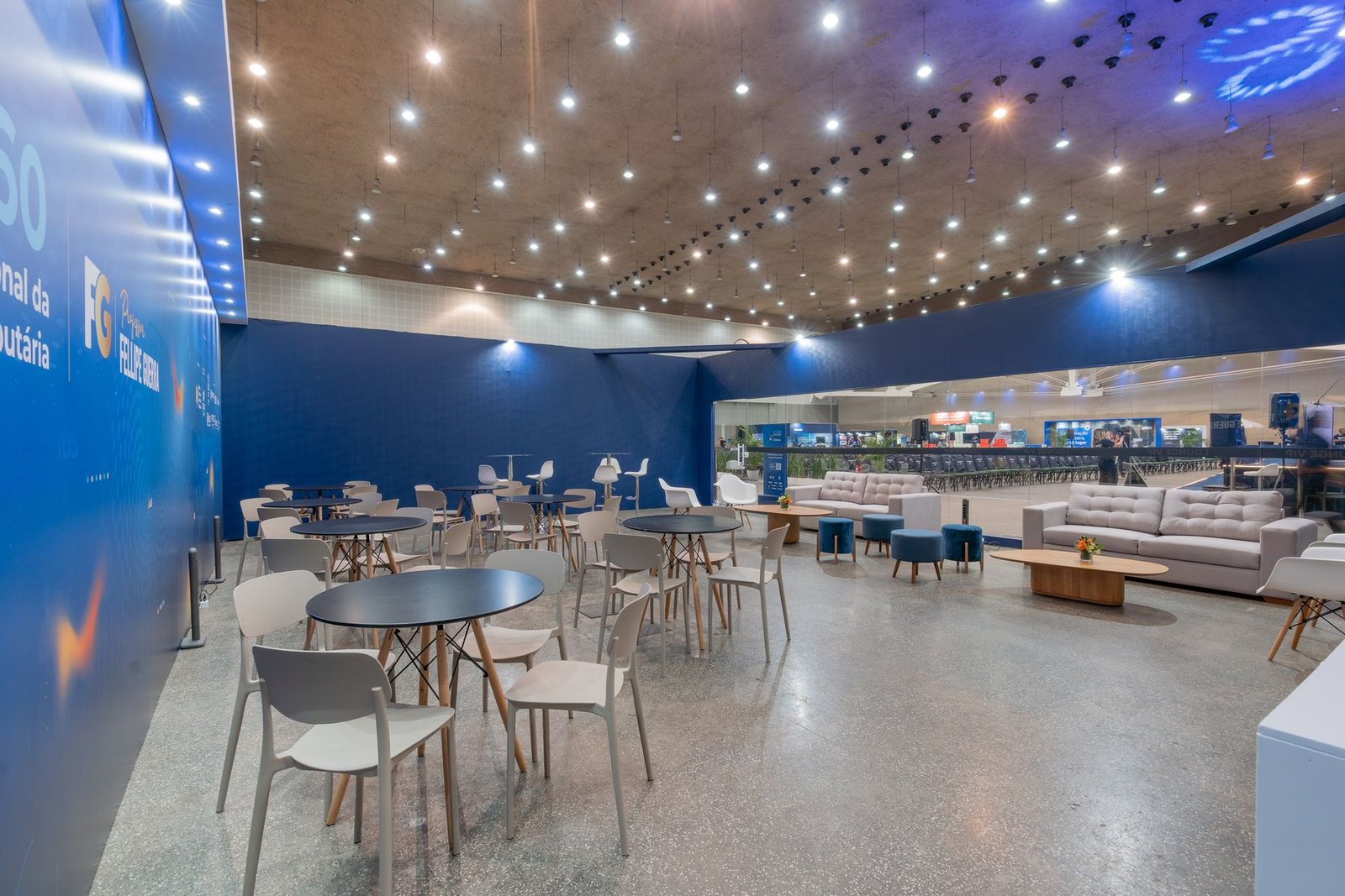 Lounge do evento com poltronas brancas e parede cenográfica azul iluminada