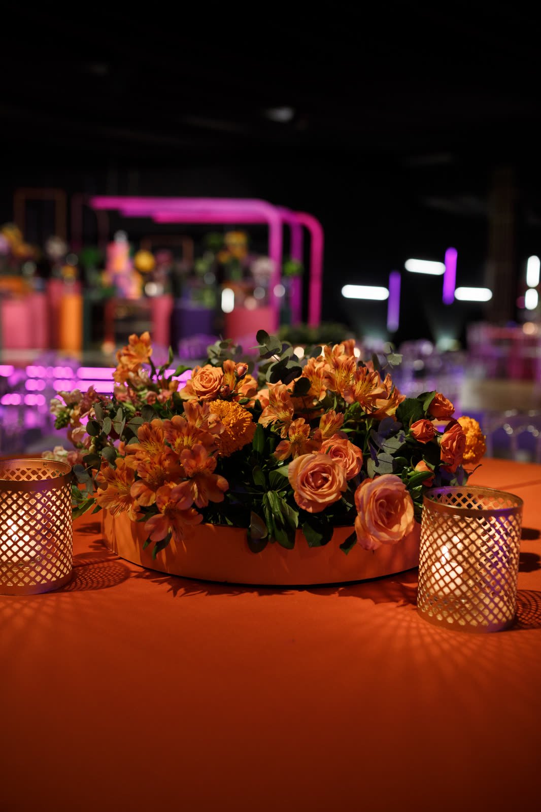 Arranjo de rosas laranja e flores do campo sobre toalha laranja, com castiçais dourados