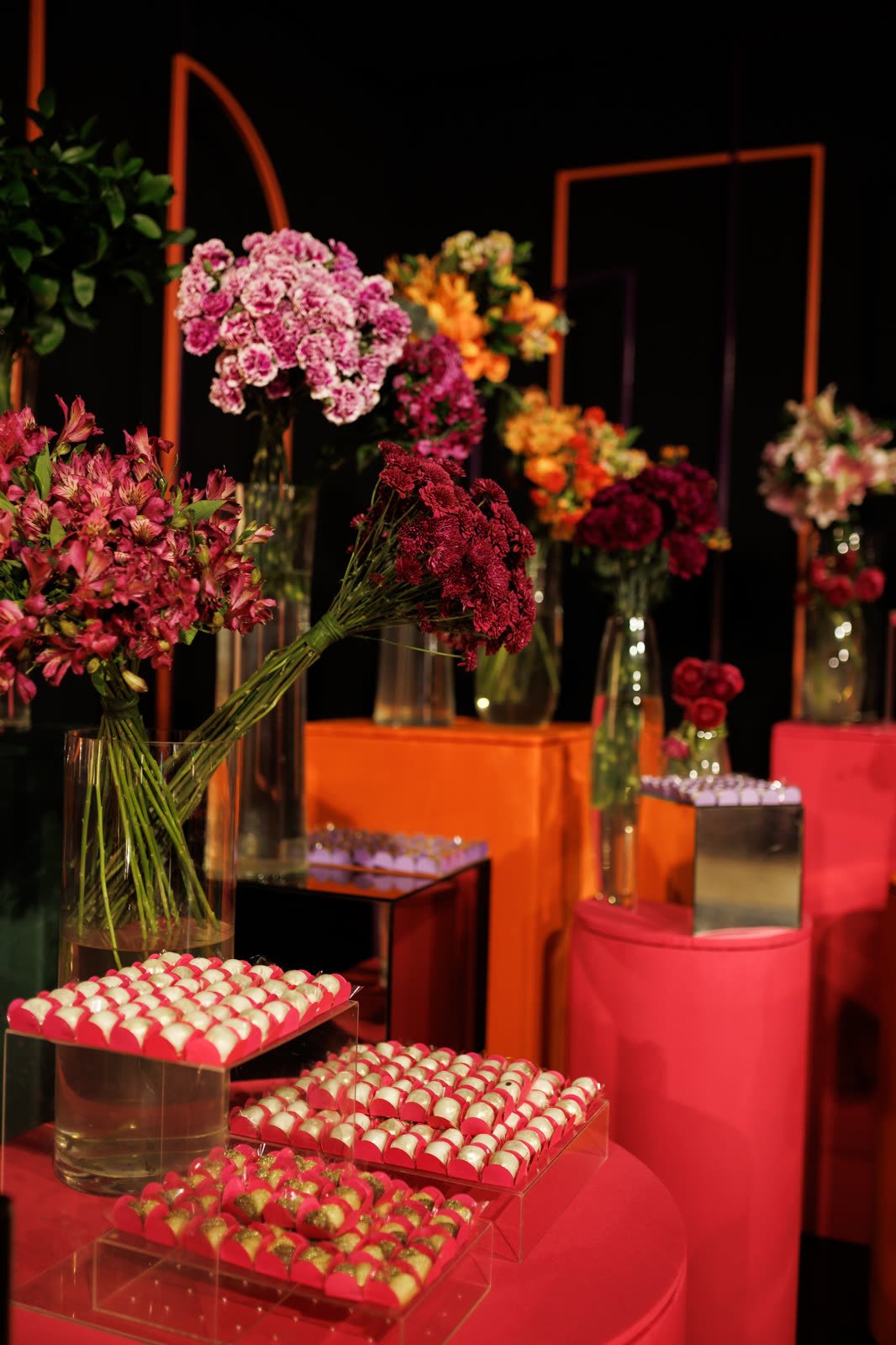 Mesa de doces com bandejas de brigadeiros e arranjos de orquídeas e rosas