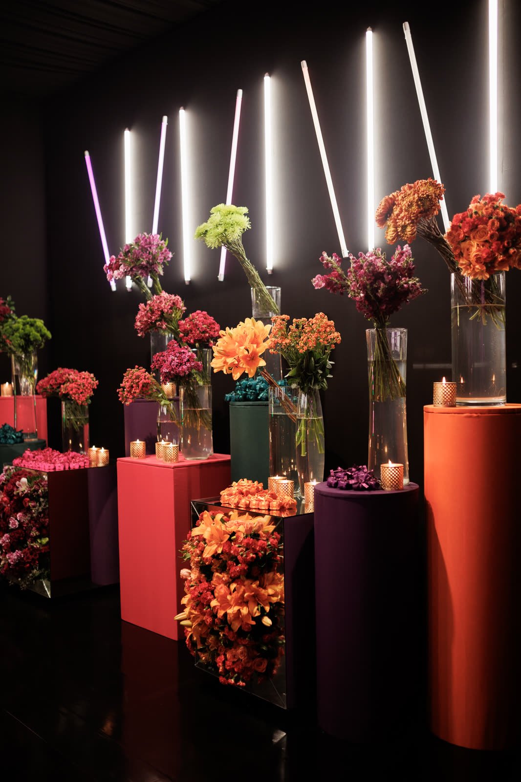 Cilindros coloridos com arranjos de flores e tubos de luz branca