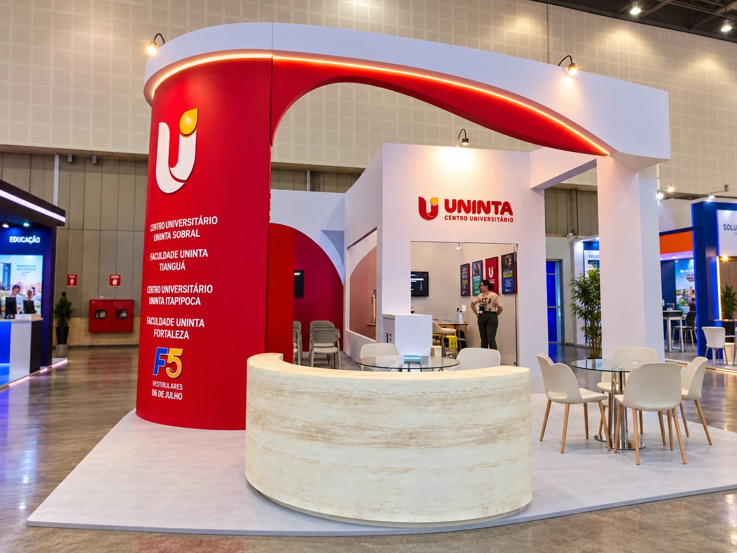 Stand da Uninta com arco vermelho, balcão curvo claro e área de mesas